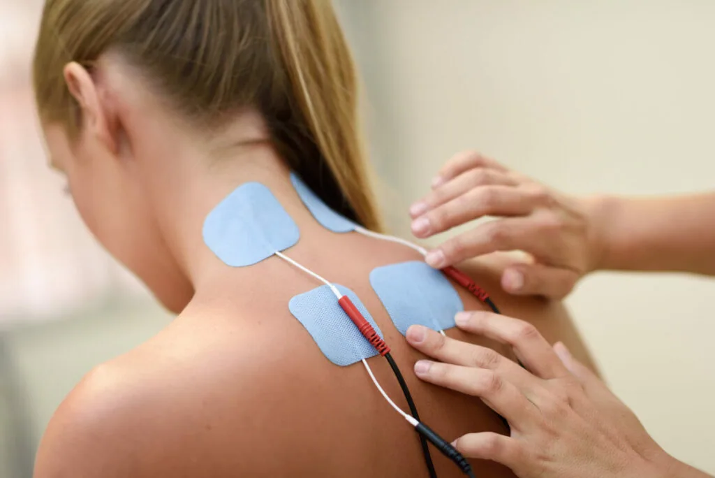 Practitioner applying blue electrode pads to patient's back for electrical stimulation therapy